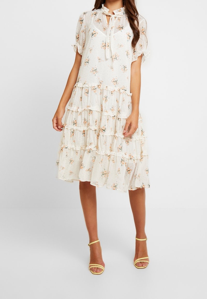 Blumen-Midi-Kleid mit gestuften Rüschen, cremefarbenem Hintergrund, zarten Blumen, kurzen, flatternden Ärmeln und einer Bindeschnürung am Hals. Kombiniere es mit gelben Absätzen.