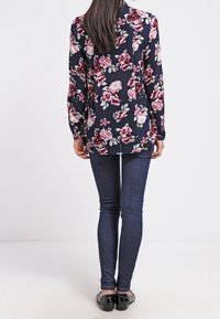 Blusa floreale con sfondo blu navy, maniche lunghe e taglio dritto; abbinata a jeans skinny di denim scuro e ballerine nere.