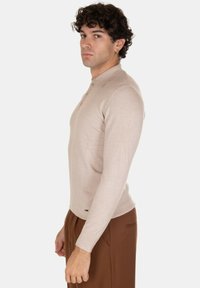 Polo shirt a maniche lunghe beige con colletto e tre bottoni. Realizzato in un materiale a maglia liscia con un design aderente.