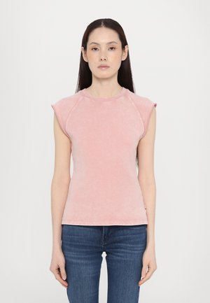 T-shirt en coton rose clair avec des manches courtes, un col rond et une texture subtile ; associé à un jean en denim bleu.