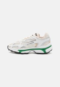 White sneaker with grey and beige mesh panels, silver accents, green midsole, and black textured rubber outsole. Features lace-up closure.