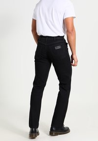 Black denim jeans with a fitted shape, featuring back pockets and a leather logo patch. Worn with a plain white shirt and black boots.