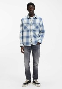 Geruit overhemd in lichtblauwe tinten, gemaakt van zachte stof met twee borstzakken, gecombineerd met vervaagde grijze spijkerbroek en zwarte sneakers.