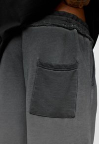 Grijze trainingsbroek met een gestructureerde afwerking, voorzien van een elastische tailleband en een enkele zijzak van bijpassende donkere stof.