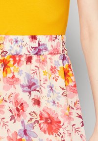 Nahaufnahme eines geblümten Rocks mit pinken, violetten, gelben und roten Blumen, kombiniert mit einem gelben Oberteil, das den elastischen Bund und einen Teil eines Armes zeigt.