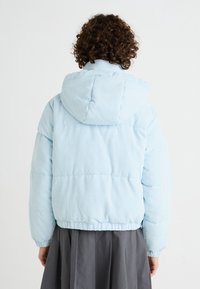 Himmelblaues Cord-Polyester-Puffermantel mit Kapuze, präsentiert mit vertikalen Streifen und elastischen Bündchen, kombiniert mit einem dunkelgrauen Rock.