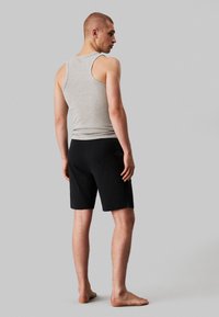 Grijze mouwloze tanktop en zwarte shorts. De tanktop heeft een geribbelde textuur. De shorts zijn soepel met een relaxte pasvorm en een elastische tailleband.