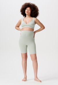 Lichtgroene geribde crop top met een v-hals en bijpassende hoge biker shorts. Gladde textuur, aansluitend ontwerp. Draagt met slippers.