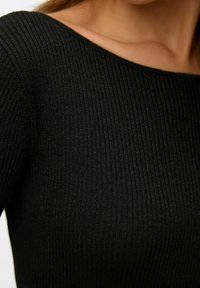 Melna ribota adīta augšdaļa ar plašu apkakli un smalku tekstūru, uzsverot pieguļošu dizainu ar vertikālām līnijām.