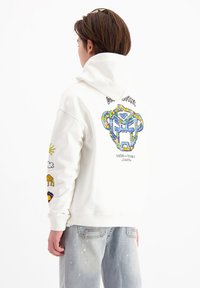 Witte hoodie met kleurrijke grafische print van een gestileerde leeuw op de achterkant, met aanvullende kleine graphics op de mouwen.