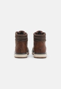 Botas de cuero marrón con un collar acolchado, cremallera en la parte trasera y costuras blancas contrastantes en la suela. Acabado texturizado y diseño robusto.