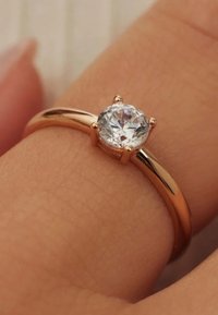 Roségoldring mit glattem Band, ausgestattet mit einem runden, klaren Diamanten, der in einer Vierkrallensetzweise gefasst ist und an einem Finger ruht.