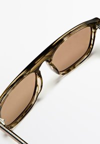 Zonnebril met bruine glazen en een oversized rechthoekig montuur in een gevlekt patroon, met dikke zijkanten en zilveren metalen accenten.