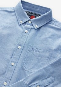Lichtblauw button-up overhemd van katoen, met een kraag, witte knopen, een borstzak met geborduurd logo en subtiele textuur.