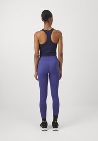 Marineblå racerback treningstop med lilla høy midje tights. Begge plaggene har en glatt tekstur og en tettsittende design. Svarte joggesko fullfører antrekket.