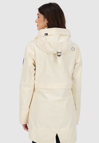 Cremfarbige wasserdichte Jacke mit hohem Kragen, verstellbarem Kapuze und Rückenbelüftung. Verfügt über eine taillierte Passform und einen reflektierenden Akzent auf der Rückseite.