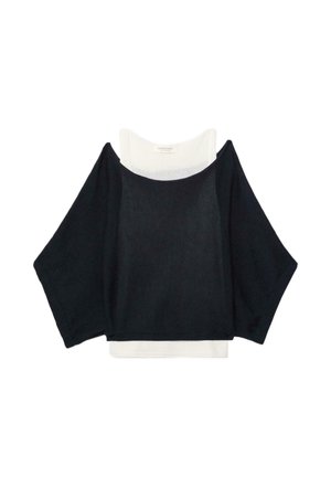 Sort løstsiddende langærmet sweater lagdelt over en hvid tætsiddende ærmeløs top, vist på en hvid baggrund.
