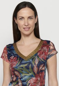 Top de patrón floral multicolor con diseño de escote en V y mangas cortas. Presenta un ribete en texturizado dorado en el escote. Tejido elástico.