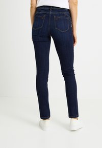 Vaqueros ajustados de color azul oscuro con una textura suave y diseño tradicional de cinco bolsillos, con costuras en contraste y un ligero elasticidad.