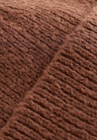 Textile tricoté brun avec une texture douce et duveteuse. Présente des sections alternées côtelées et lisses, ce qui améliore le détail tactile.