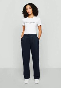 Un tricou alb din bumbac cu logo imprimat, asortat cu pantaloni bleumarin cu croială dreaptă și buzunare laterale. Purtați cu adidași albi.