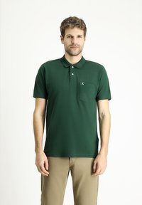 Polo verde a maniche corte, con colletto, tre bottoni e taschino sul petto. Il tessuto appare liscio e ha un colore uniforme senza motivi.