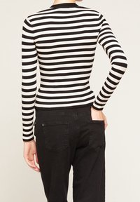 Svart- och vitrandig långärmad ribbad topp med figurnära passform. Bärs med svarta byxor som har två bakfickor och en enkel midjeband.