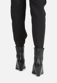 Bottines noires à talon compensé en cuir, avec une texture lisse, un col doux et des détails de couture apparente, présentant un design à bout rond.