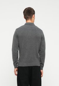 Suéter gris de punto con cuello, que presenta una tela texturada, dobladillo acanalado y mangas largas, mostrado desde la parte de atrás.