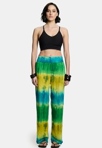Czarny stanik sportowy połączony z luźnymi spodniami w stylu tie-dye w zielonych, żółtych i niebieskich odcieniach. Miękka tkanina z elastycznym pasem i prostymi nogawkami.