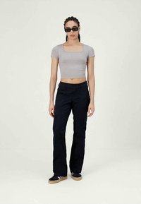 Siva kratka srajca, visokopasne mornarsko modre hlače z žepi za tovor in črni supergi z bež podplati. Videz dopolnjujejo temna sončna očala.