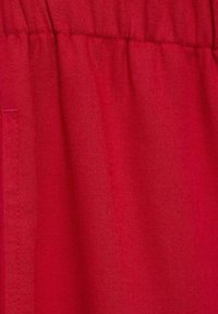 Rdečo blago z gladko teksturo, ki vključuje subtilne gubice in nabrano elastično pasico, primerno za oblikovanje oblačil.