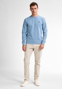 Felpa azzurra con collo rotondo e maniche lunghe, dotata di un piccolo logo. Abbinata a pantaloni beige e sneakers bianche.