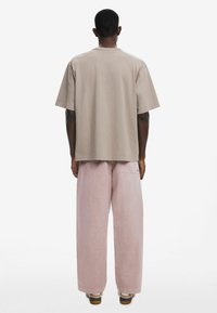 Beige bavlněné tričko s krátkým rukávem, doplněné volnými růžovými kalhotami, předvádějícími jemnou texturu a minimalistický design.
