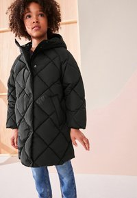 Cămașă puffer neagră, matlasată, cu glugă, având un model în diamond și închidere cu nasturi pe față. Purtați peste blugi albaștri, în interior, cu un fundal neutru.