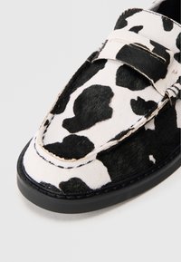 Mustvalge lehma nahast loafers, millel on ümar nina, lame talla ja õmmeldud detailid koos siledaga tekstuuriga.