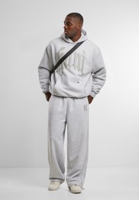 Gray hoodie with large silver text, matching gray sweatpants, and cream sneakers, worn with a black crossbody bag. Smooth fabric and relaxed fit.