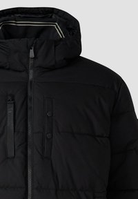 Schwarze gepolsterte Winterjacke mit hohem Kragen, Frontreißverschluss, Brusttasche mit Druckknopf und abnehmbarer Kapuze mit reflektierendem Besatz.