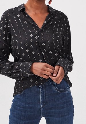 Schwarze Bluse mit Kragen, die ein kleines, wiederholendes Blumenmuster in Weiß und Braun aufweist. Lange Ärmel, Knopfmanschetten und glattes, glänzendes Material.