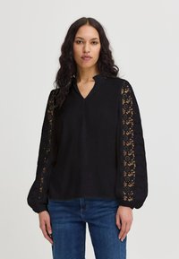 Blusa nera con scollo a V e dettagli in pizzo sulle maniche lunghe. Presenta una vestibilità morbida e un tessuto testurizzato con polsini arricciati.
