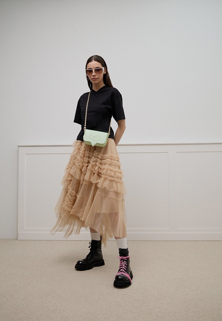 Top negro de manga corta, falda de tul beige en capas con volantes, bolsa de hombro verde menta y botas negras con cordones rosas.