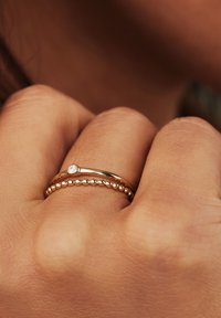 Goldringe, die übereinander auf einer Hand gestapelt sind; einer hat einen kleinen Diamanten, der andere ein Perlenmuster. Glatte und polierte Metalloberfläche.