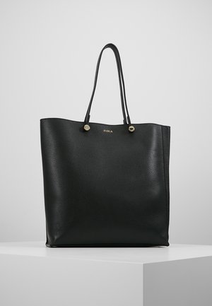 Sac cabas en cuir noir texturé avec deux fines bretelles et petits détails dorés de logo et bouton sur un socle d'exposition blanc.