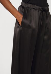 Svarta satinbyxor med elastisk midja och dragsko, med sidfickor och en slät, glansig yta.