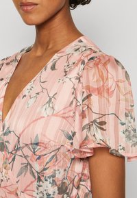 Floral dress with a deep V-neck, short puff sleeves, and a lightweight pink fabric adorned with delicate botanical patterns and subtle stripes.