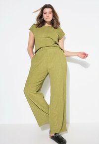 Olijfgroene, textuurvolle twee-delige outfit met een top met korte mouwen en ruime broek met een subtiel patroon. Zwarte instappers.