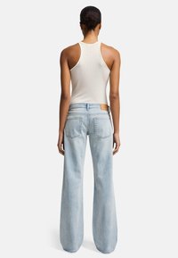 Jeans a gamba larga di un azzurro chiaro realizzati in denim con una finitura morbida, abbinati a una canotta a coste di colore crema, che evidenzia una vestibilità rilassata e tasche posteriori.