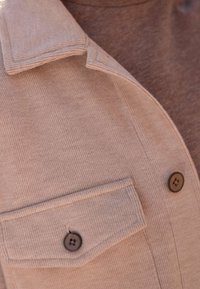 Close-up van een beige corduroy jackzak met een knop, met zichtbare kraag en knopdetails op de gestructureerde stof.