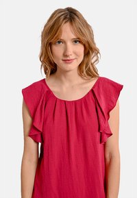 Top senza maniche fucsia con dettagli arricciati lungo le spalle, realizzato in tessuto testurizzato con una vestibilità leggermente ampia.