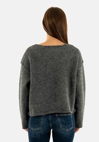 Maglione grigio in lana con scollo ampio, maniche a goccia e vestibilità morbida. Texture soffice, stile informale e orlo posteriore leggermente accorciato.